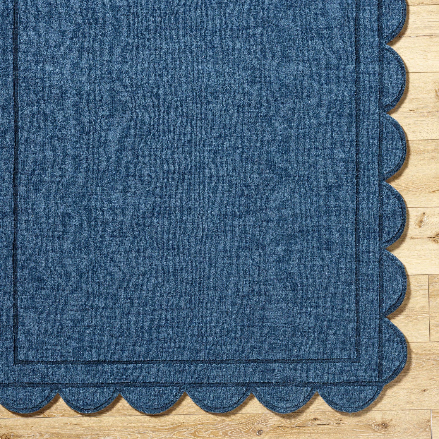 Close-up of the hand-loomed Uhuro Blue Geometric Area Rug showing its wool texture and scalloped edge detail. Corner