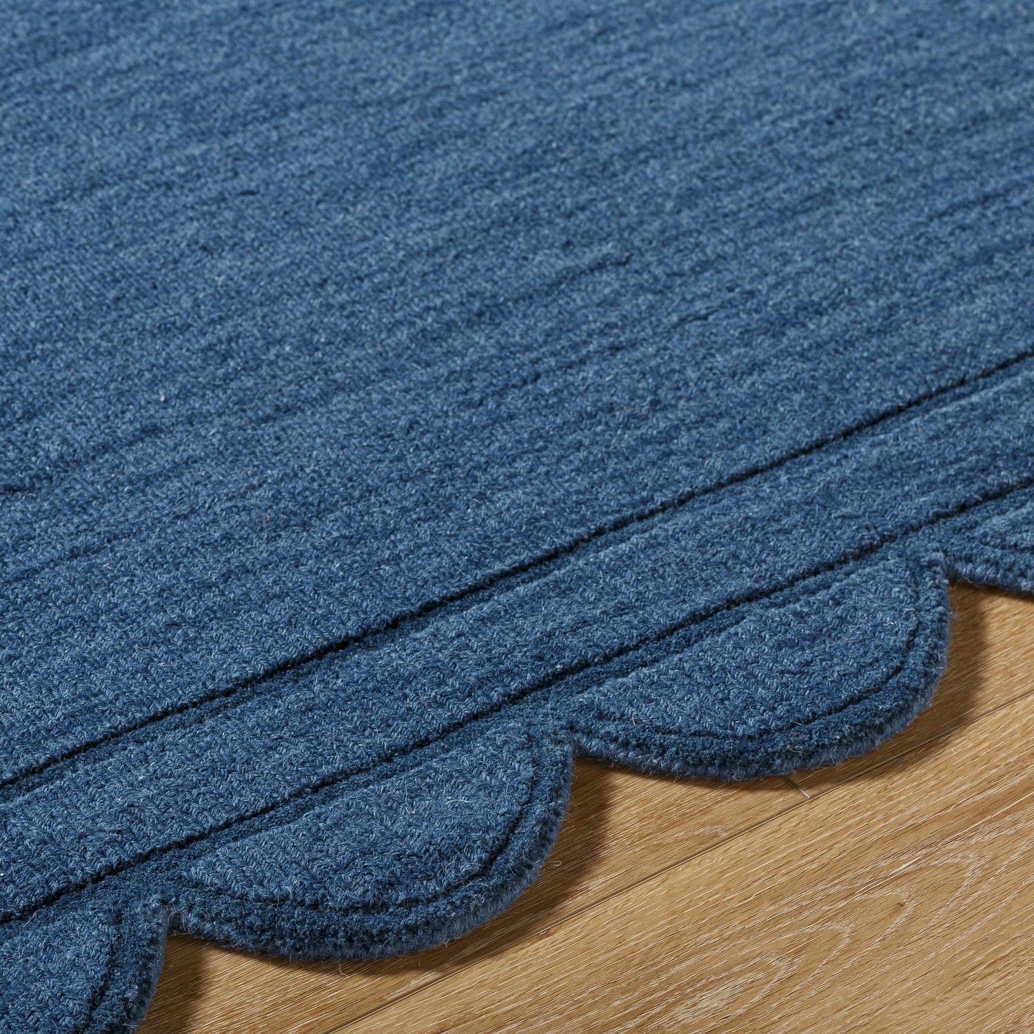 Close-up of the hand-loomed Uhuro Blue Geometric Area Rug showing wool texture and the rug's unique scalloped edge. Texture