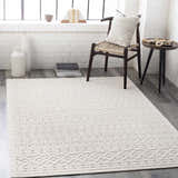 Living room scene with a cream Maribyrnong 3D Outdoor Area Rug, chair, and side table against a white brick wall. Roomscene-Rectangle