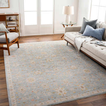 Living room scene with a Mira Thick Luxe Oushak Rug, beige sofa, wood floors, and natural light. The rug adds a touch of traditional style. Roomscene-Rectangle