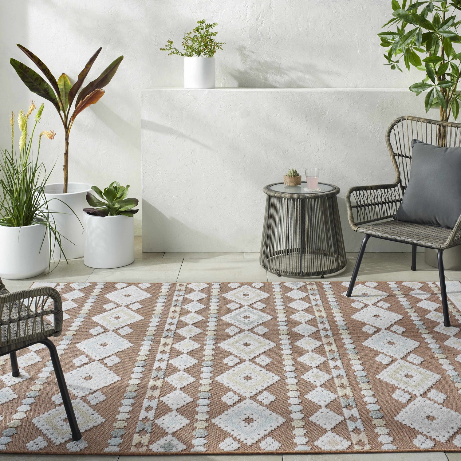 Coastal patio scene with Metta Rust Area Rug, woven chairs, side table, and potted plants. Roomscene-Rectangle