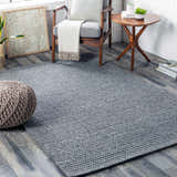 Living room scene with a medium gray Mulgoa Area Rug, gray chair, wood side table, and a knit pouf. Roomscene-Rectangle