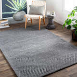 Contemporary living room scene with a gray hand woven Mulgoa Area Rug, chair, side table, and plant. Roomscene-Rectangle