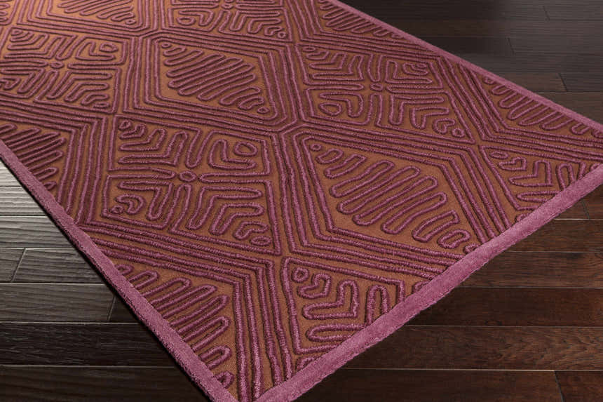 Close-up of the hand woven Mylo Area Rug. Burnt orange wool rug with mauve geometric pattern and border. Corner