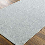 Close-up of the Mirit Area Rug. Denim and light gray woven texture on a rectangle rug. Corner