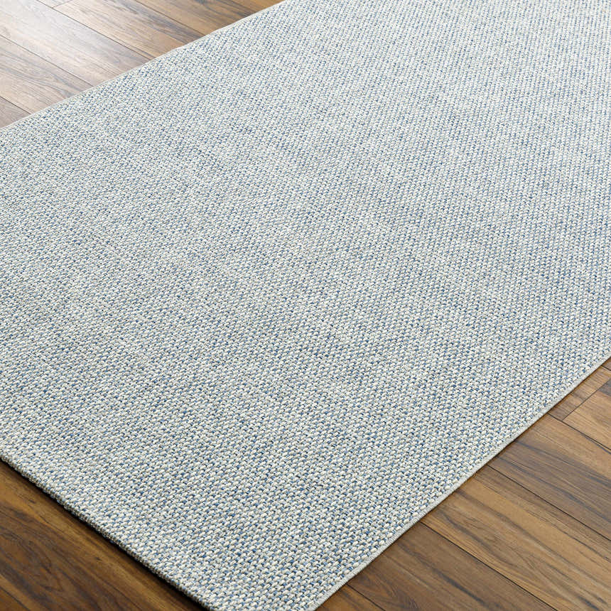 Close-up of the Mirit Area Rug. Denim and light gray woven texture on a rectangle rug. Corner