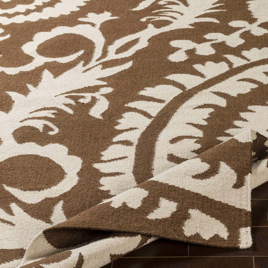 Close-up of the hand woven Naeva Area Rug. Dark brown and walnut floral pattern on 100% wool texture. Fold