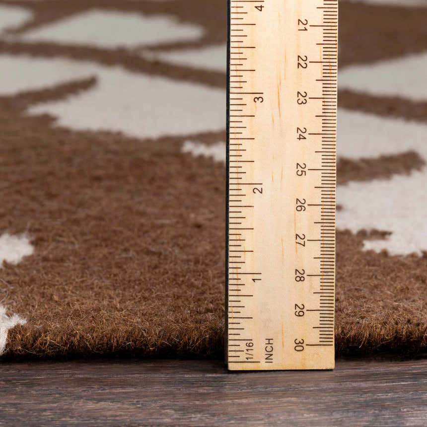 Close-up of Naeva Area Rug showing the pile height with a ruler. Brown wool rug with a cream pattern. Pile