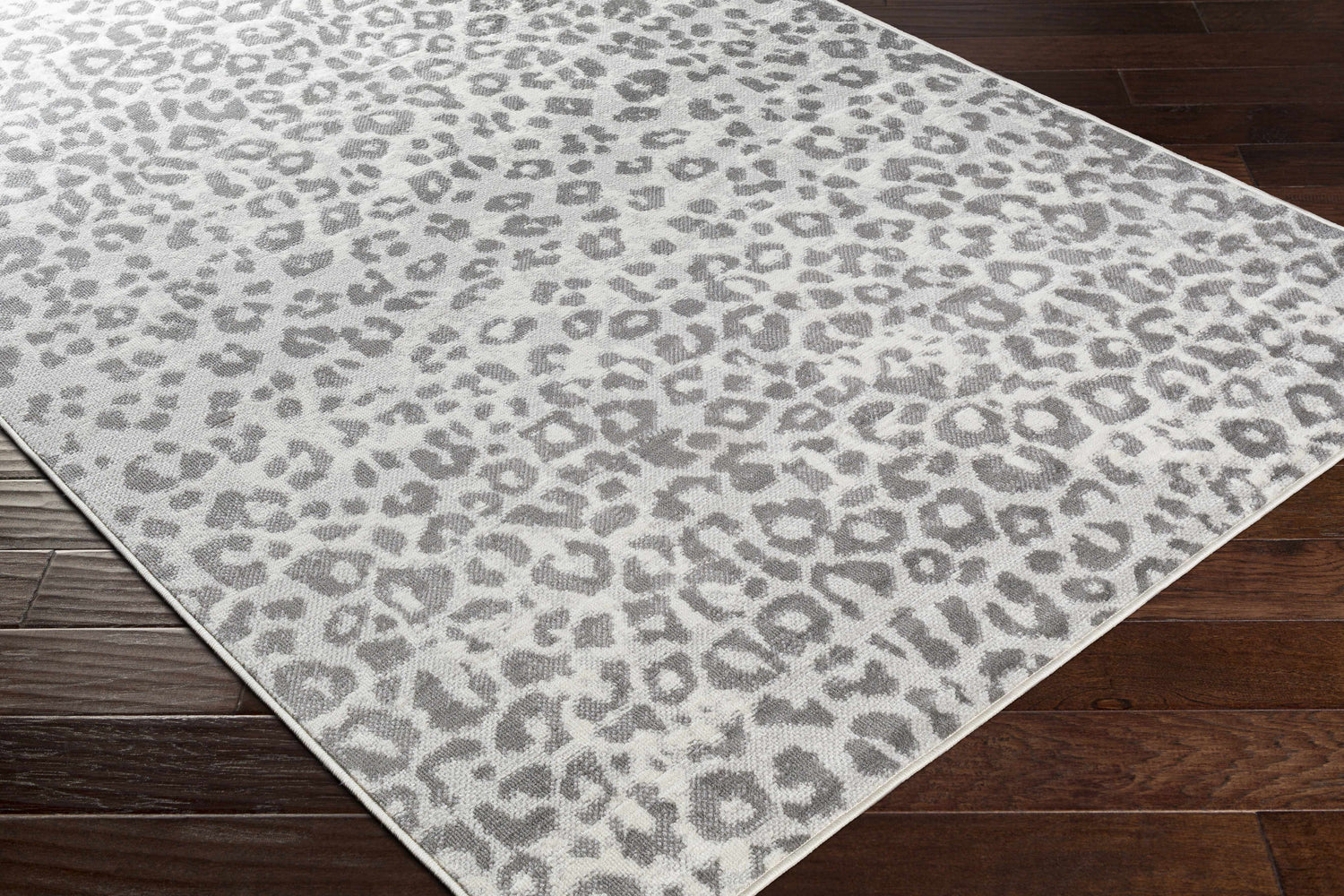 Close-up of the Nagambie Leopard Print Area Rug. Gray animal print rug on a dark wood floor. Corner
