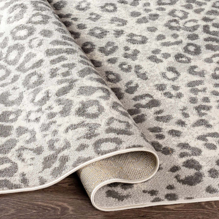 Close-up of the Nagambie Leopard Print Area Rug. Features a gray leopard pattern on a light gray, machine-woven pile. Fold