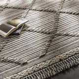 Close-up of the Nairobi Area Rug: black and ivory striped wool rug with knotted fringe and a book on top. Styleshot