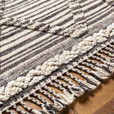 Close-up of the Nairobi Area Rug, a hand-knotted wool rug with black, gray, and ivory stripes and braided fringe. Texture