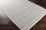Close-up of Nalcrest Washable Area Rug. White and gray cotton rug with a geometric, bohemian-inspired pattern. Machine woven texture. Corner
