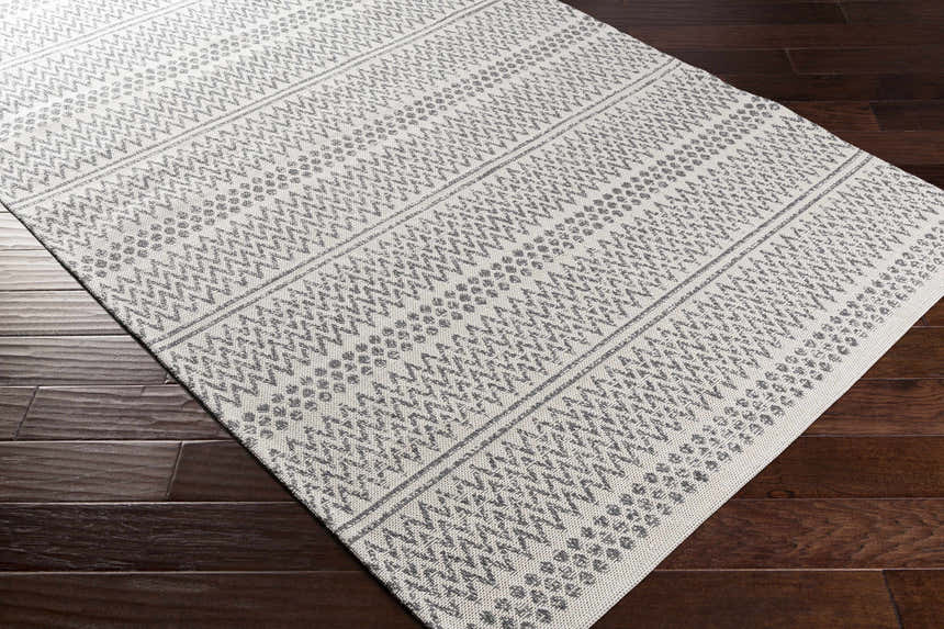 Close-up of Nalcrest Washable Area Rug. White and gray cotton rug with a geometric, bohemian-inspired pattern. Machine woven texture. Corner