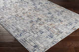 Close-up of Nalus Area Rug with a cream, denim, and brick red geometric pattern on dark wood flooring. Corner