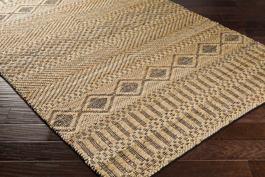 Close-up of tan and black Nasugbu Jute Carpet. Hand-woven geometric design on dark wood floor. Bohemian farmhouse style. Corner