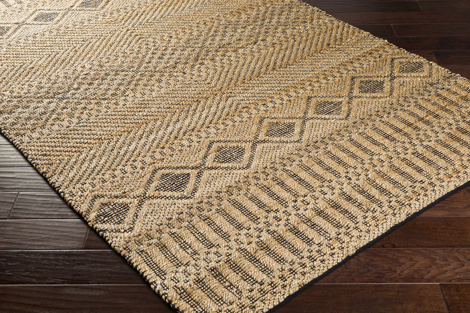 Close-up of tan and black Nasugbu Jute Carpet. Hand-woven geometric design on dark wood floor. Bohemian farmhouse style. Corner