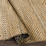 Close-up of the hand woven Nasugbu Jute Carpet. Tan jute rug with a subtle black geometric pattern and natural texture. Fold