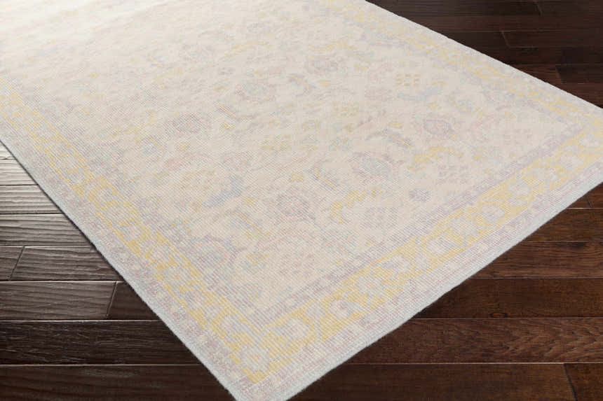 Close-up of the hand-knotted Navarino Area Rug, a traditional design in light beige, dusty pink, and mustard on dark wood floors. Corner