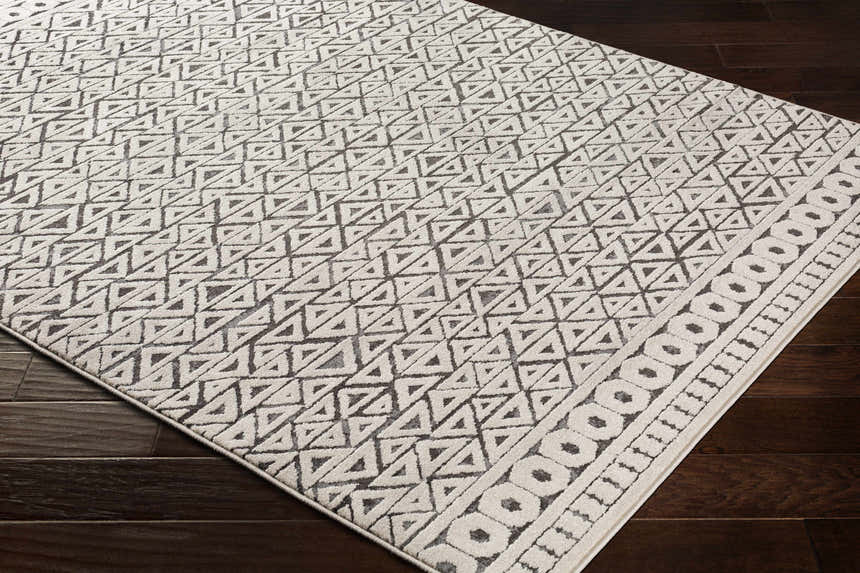 Close-up of the Naylor Beige/Charcoal Rug. Features a geometric triangle pattern and a border of circles. Farmhouse style. Corner