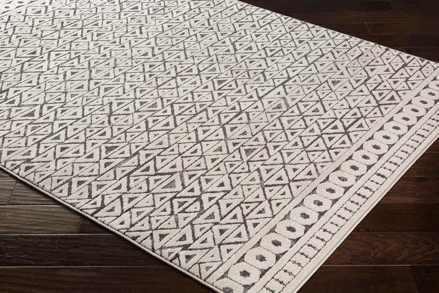 Close-up of the Naylor Beige/Charcoal Rug. Features a geometric triangle pattern and a border of circles. Farmhouse style. Corner