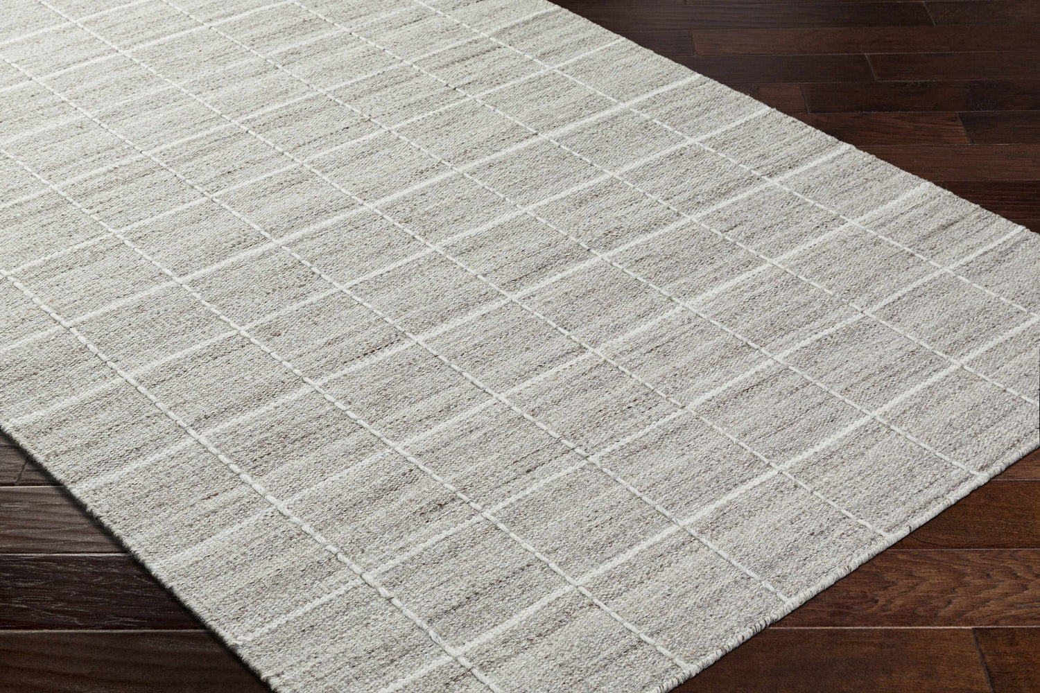 Close-up of the hand-woven Nissa Checkered Area Rug. Light gray wool rug with an off-white checkered pattern. Corner