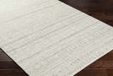 Close-up of the hand woven Nissa Tan Area Rug, a farmhouse style rug in ivory and tan wool on dark wood flooring. Corner