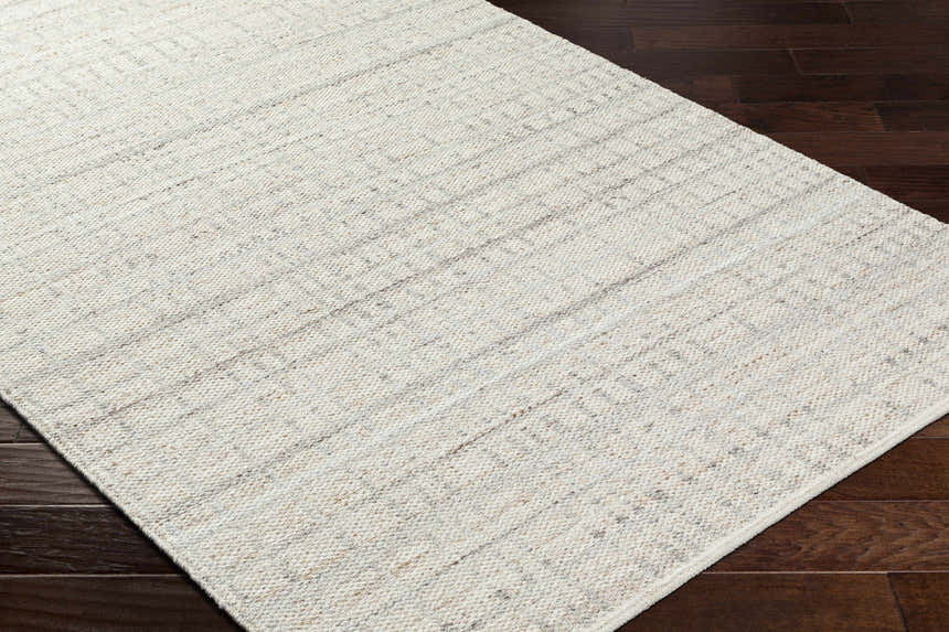 Close-up of the hand woven Nissa Tan Area Rug, a farmhouse style rug in ivory and tan wool on dark wood flooring. Corner