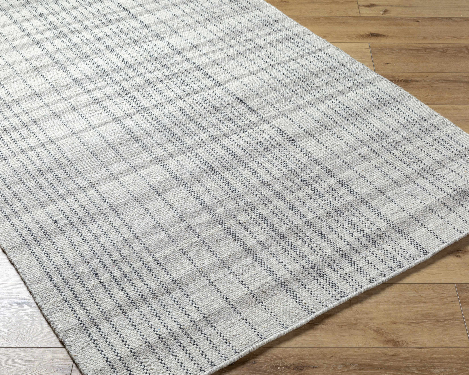 Close-up of the hand woven Nissa Blue Gray Checkered Area Rug on wood floor. Light silver, sage, and slate blue wool rug. Corner