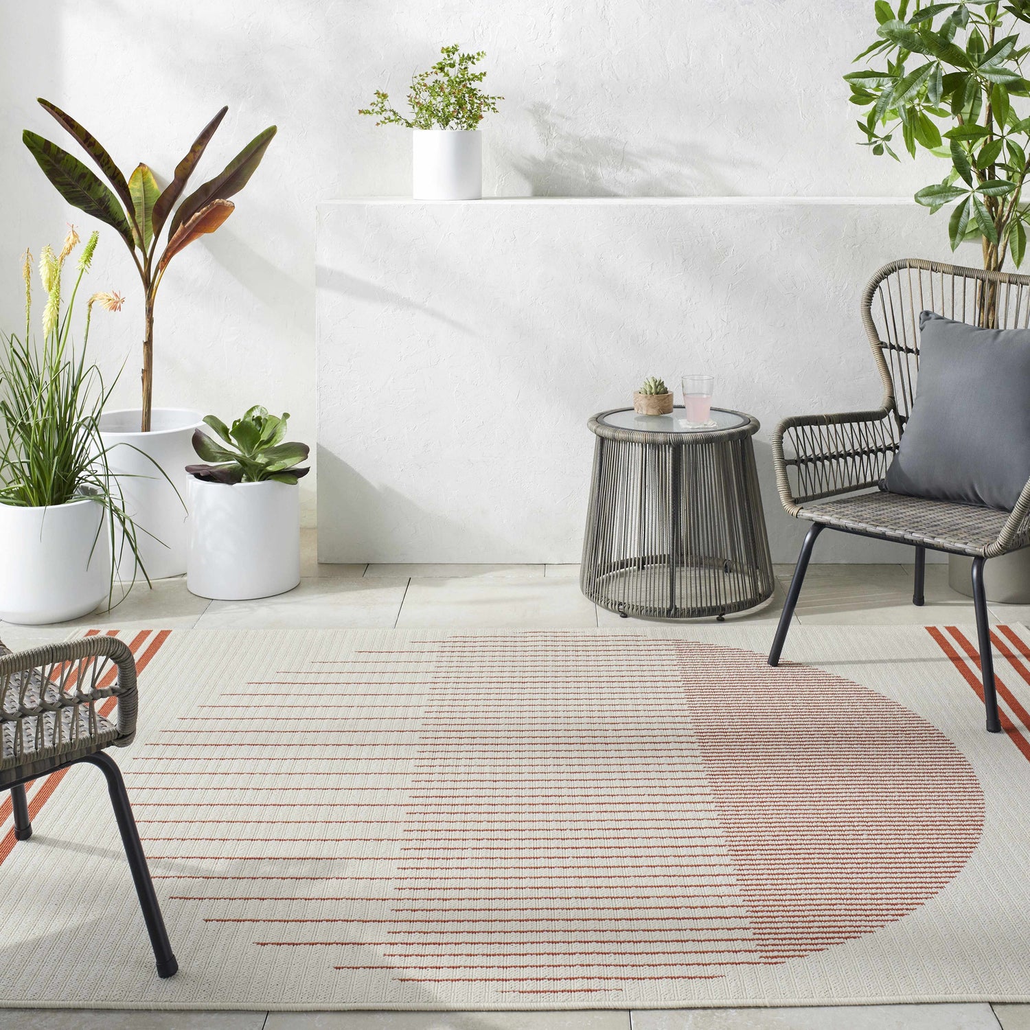 Minimalist patio scene with a cream Nabil rug featuring an orange circle design, paired with gray wicker furniture. Roomscene-Rectangle