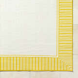 Close-up of the Nadir Area Rug. Cream rug with a yellow striped border on a tile floor. Corner