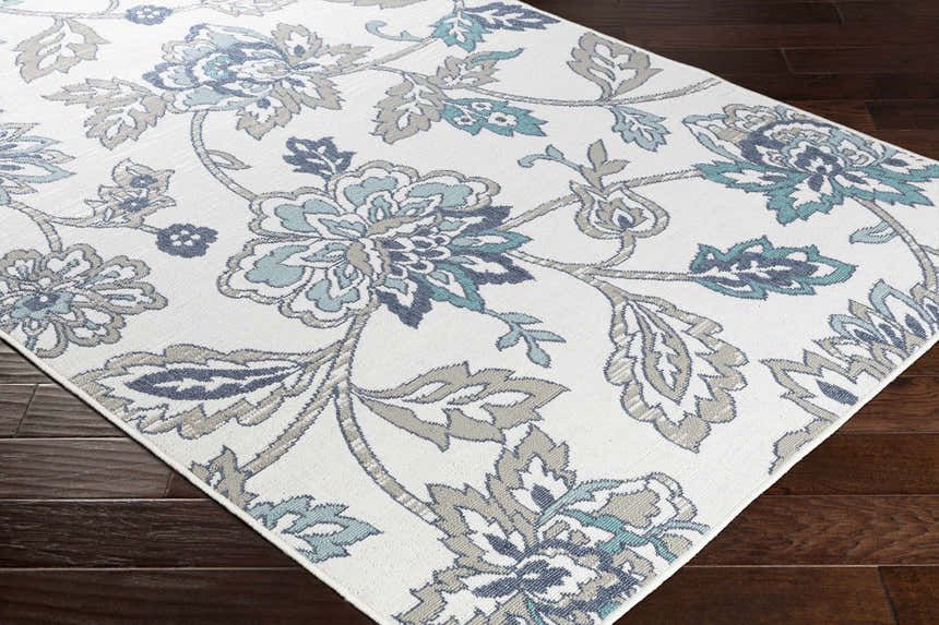 Close-up of the Neon Area Rug. White rug with navy, pale blue, taupe, and teal floral pattern. Corner