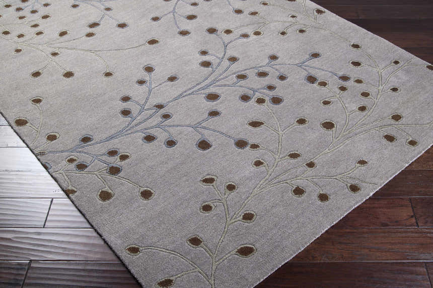 Close-up of Sage Brown Elsu Area Rug with a floral design in brown, sage, and gray on a wood floor. Corner