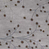 Close-up of the Sage Brown Elsu Area Rug showing its floral branch pattern in brown and sage on a gray wool texture. Swatch