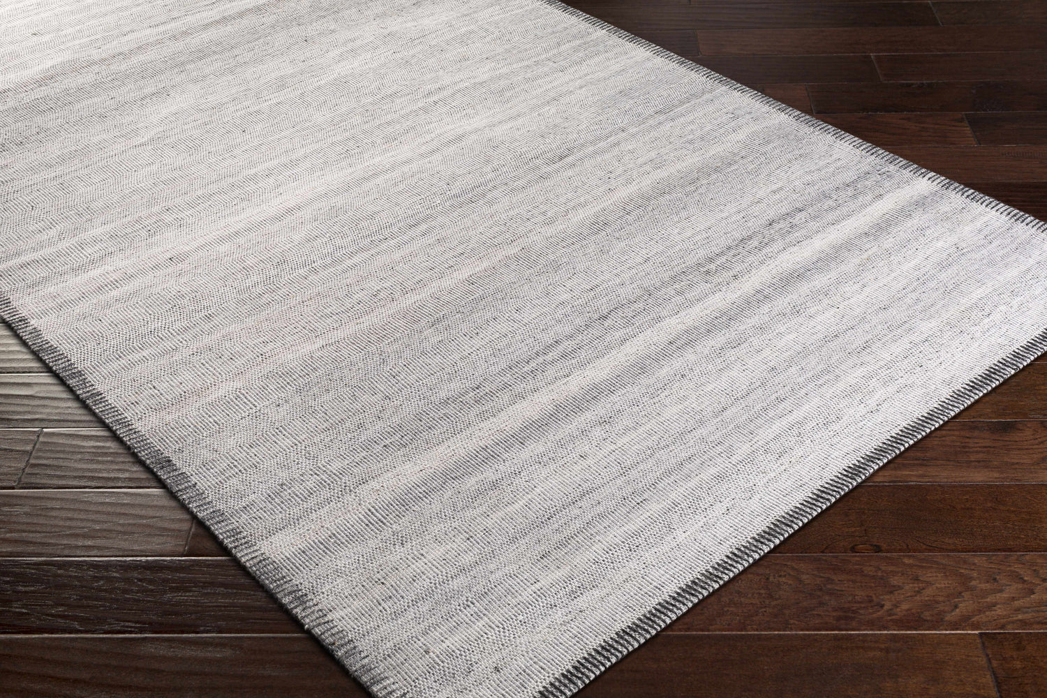 Close-up of Nettleham Silver Viscose Rug showing woven texture and charcoal, gray, and silver tones on dark wood floor. Corner
