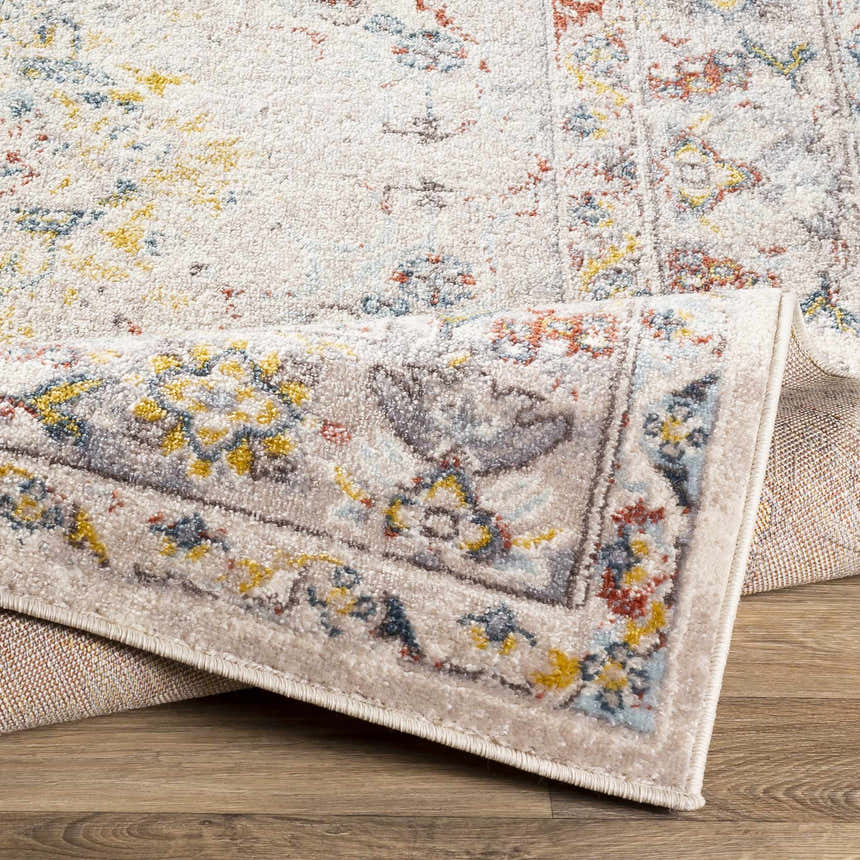 Close-up of the Newkirk Area Rug showing its cream base with brick red, charcoal, dark blue, and mustard floral pattern. Fold