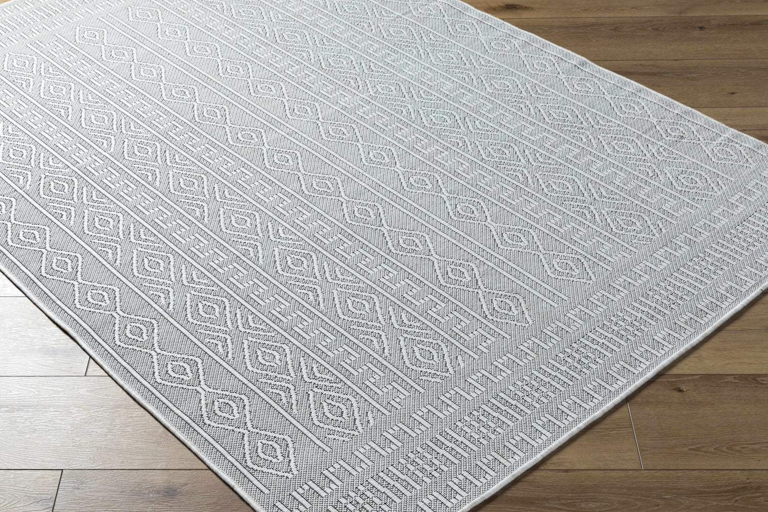 Close-up of the Nuela Light Gray Area Rug showing its diamond and line pattern and woven texture on a wood floor. Corner