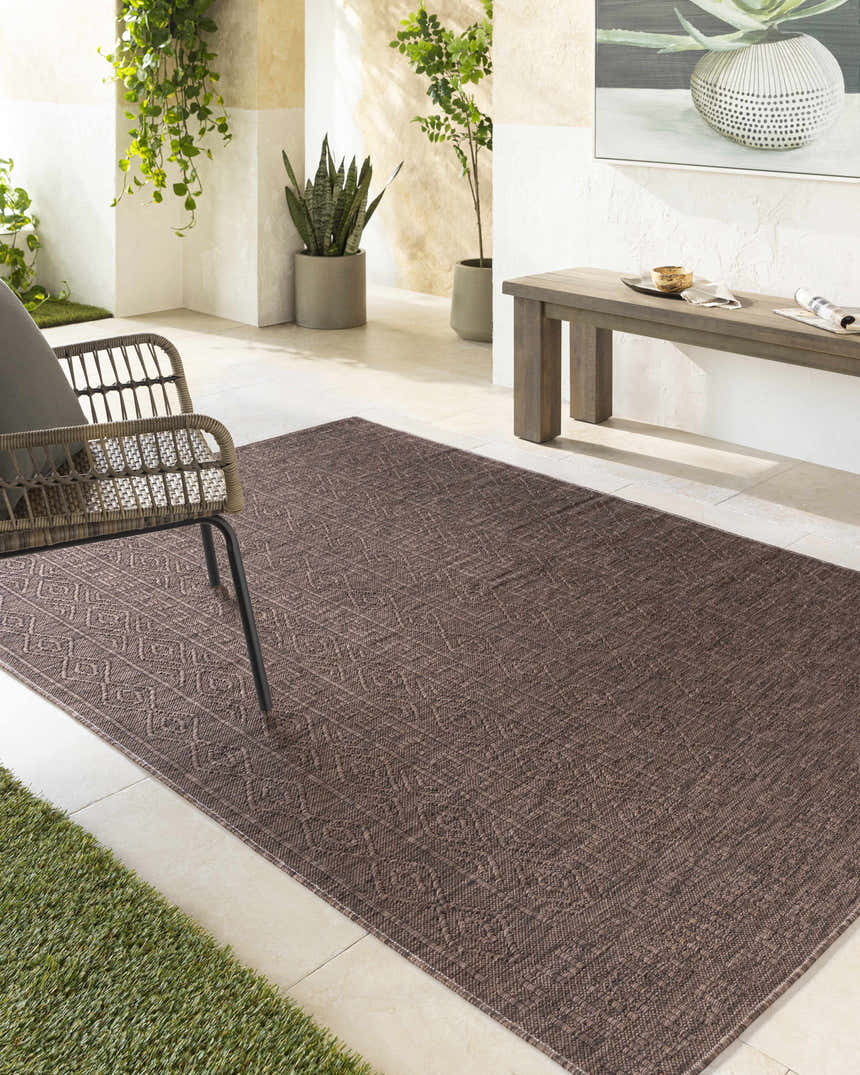 Outdoor patio scene with a Nuela Dark Brown Area Rug, wicker chair, bench, and potted plants. Roomscene-Rectangle