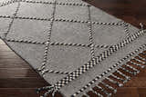 Close-up of the Ninderry Wool Area Rug. Black and cream rug with a geometric pattern and braided fringe detail. Corner