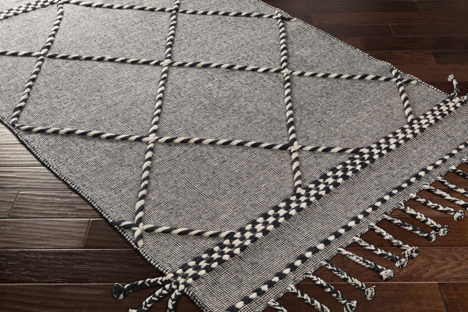 Close-up of the Ninderry Wool Area Rug. Black and cream rug with a geometric pattern and braided fringe detail. Corner