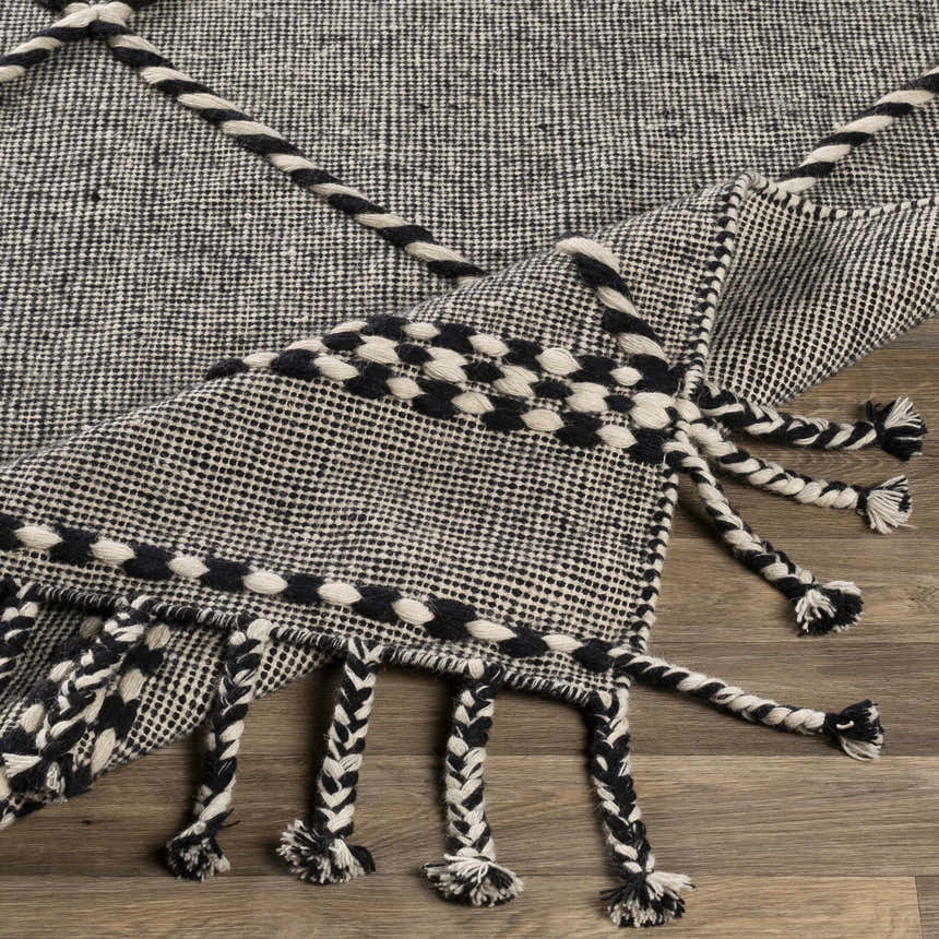 Close-up of the hand woven Ninderry Wool Area Rug. Black and cream rug with braided tassels. Bohemian farmhouse style. Fold