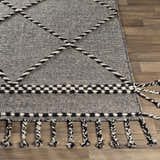 Close-up of the Ninderry Wool Area Rug showing its black and cream woven texture, braided accents, and decorative tassels. Front