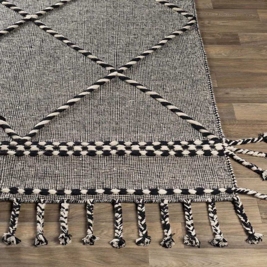 Close-up of the Ninderry Wool Area Rug showing its black and cream woven texture, braided accents, and decorative tassels. Front