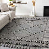 Living room scene with the Ninderry Wool Area Rug, showcasing its black and cream diamond pattern and braided fringe. Roomscene-Rectangle