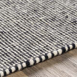 Close-up of the hand woven Ninderry Wool Area Rug. Black and cream wool creates a textured, bohemian pattern. Texture