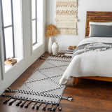 Bedroom scene with Ninderry Wool Area Rug runner in black and cream, styled with a bed, wall art, and wood floors. Roomscene-Runner