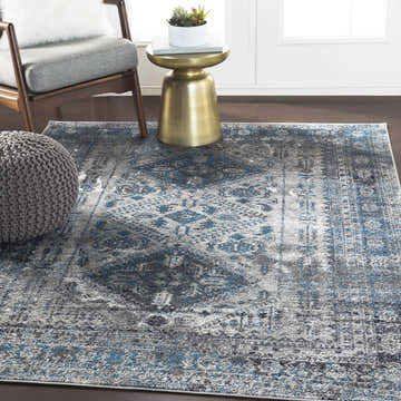 Living room scene with blue Nisula Traditional Rug, gray chair, pouf, and gold accent table. Roomscene-Rectangle
