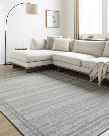 Living room scene with a gray striped Nimue Gray Area Rug, ivory sectional sofa, and wood floors. Roomscene-Rectangle