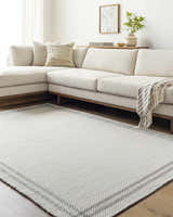 Living room with a Nimue Cream & Charcoal Bordered Area Rug, light beige sofa, and wood accents. Roomscene-Rectangle