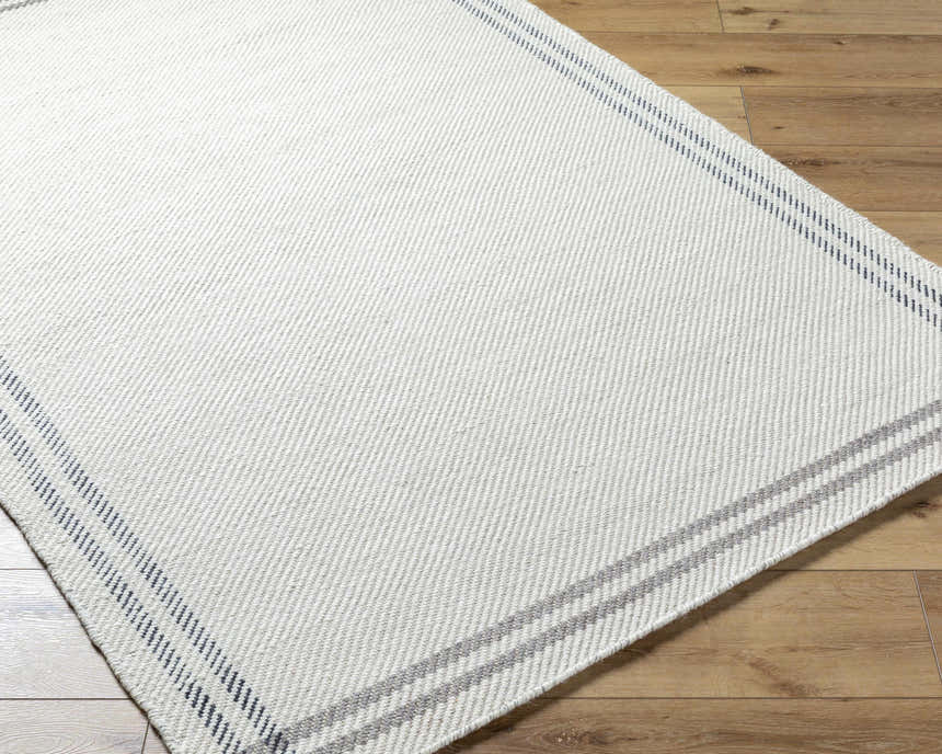 Close-up of the hand-woven Nimue Cream & Charcoal Bordered Area Rug showing its wool texture and striped border. Corner